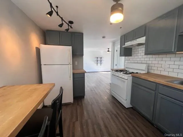 Kitchen with gray cabinets, white appliances, butcher block counters, decorative backsplash, and dark wood-type flooring Kitchen with gray cabinets, white appliances, butcher block counters, decorative backsplash, and dark wood-type flooring