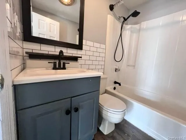 Full bathroom with shower / washtub combination, hardwood / wood-style floors, toilet, decorative backsplash, and vanity Full bathroom with shower / washtub combination, hardwood / wood-style floors, toilet, decorative backsplash, and vanity
