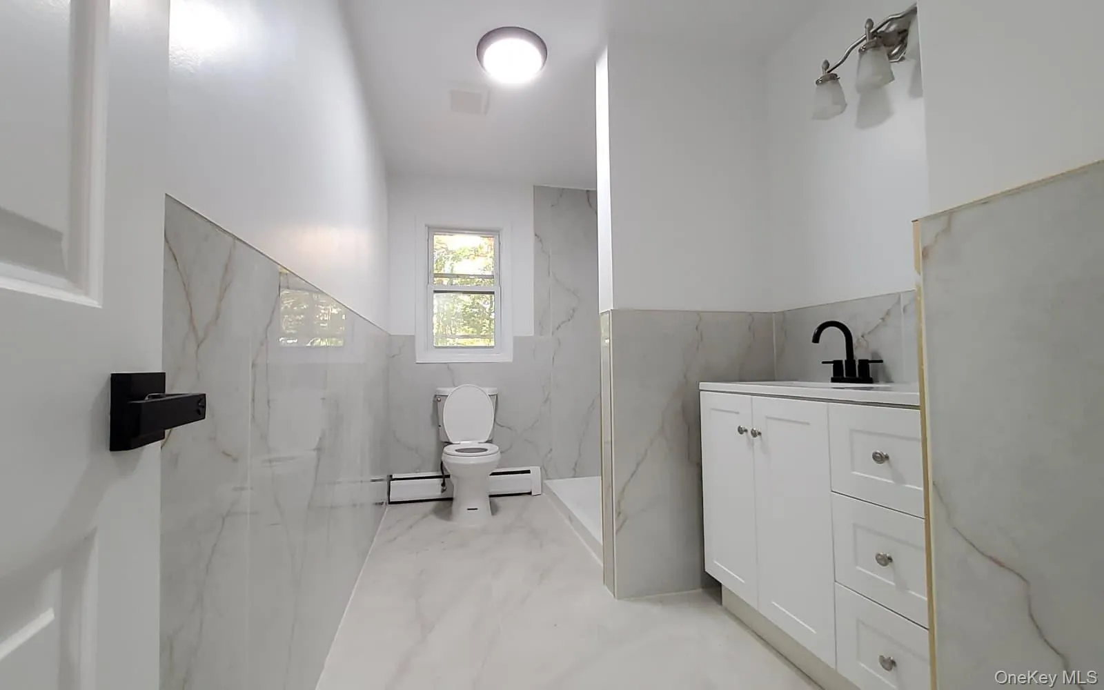 Full bath featuring light marble finish flooring, tile walls, vanity, baseboard heating, and a marble finish shower Full bath featuring light marble finish flooring, tile walls, vanity, baseboard heating, and a marble finish shower