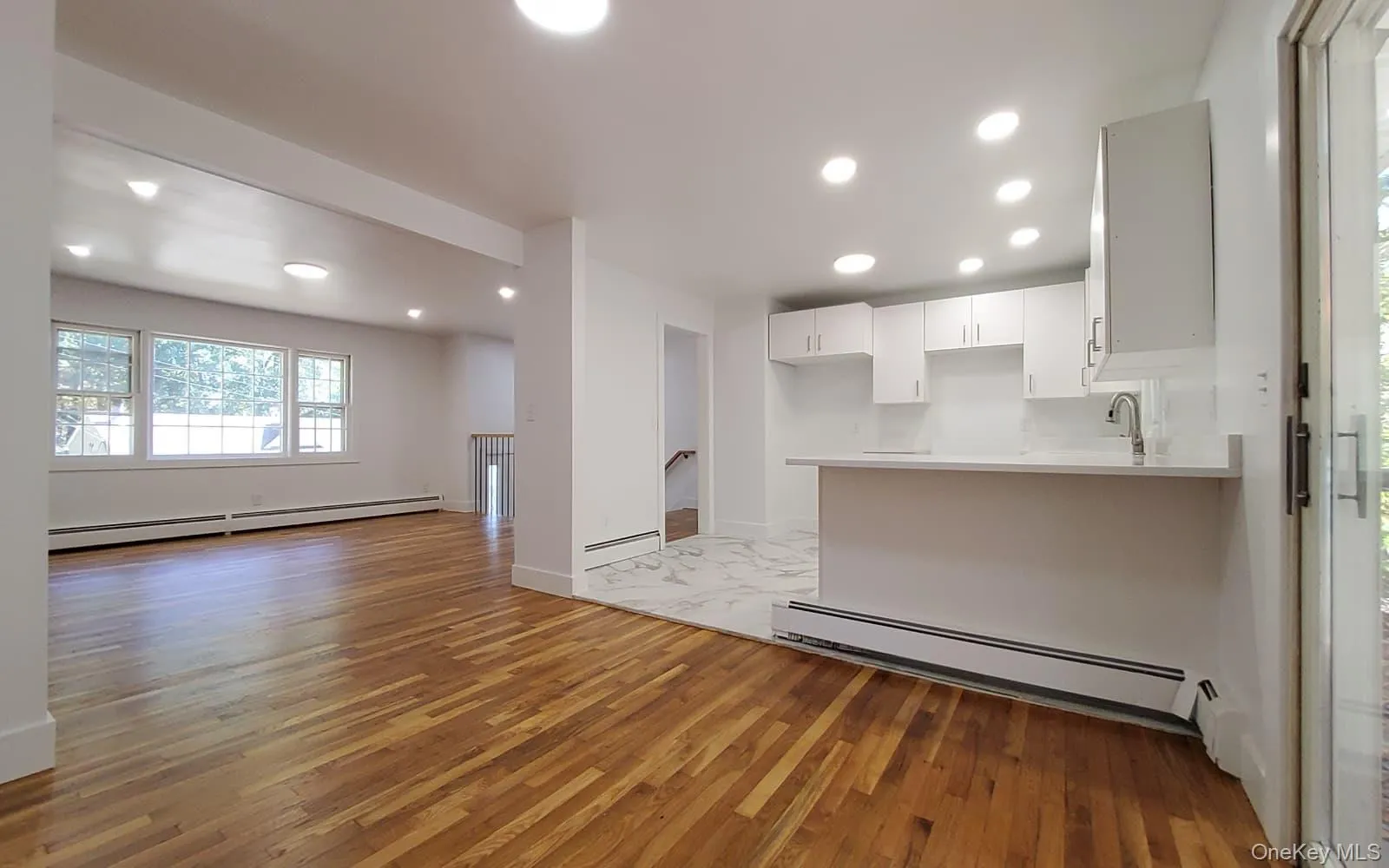 Unfurnished living room with baseboard heating, light wood-type flooring, and recessed lighting Unfurnished living room with baseboard heating, light wood-type flooring, and recessed lighting