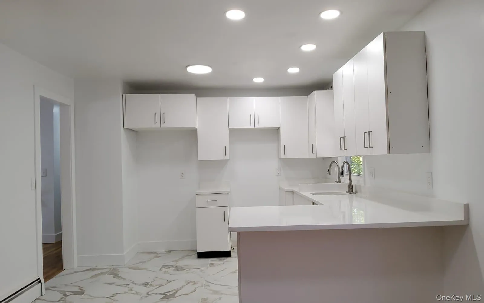 Kitchen featuring light marble finish flooring, white cabinets, a baseboard heating unit, recessed lighting, and light stone countertops Kitchen featuring light marble finish flooring, white cabinets, a baseboard heating unit, recessed lighting, and light stone countertops
