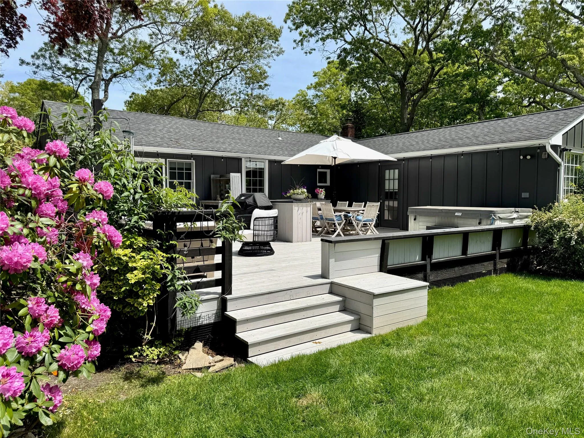 Rear view of property featuring board and batten siding, a shingled roof, a wooden deck, outdoor dining space, and a lawn Rear view of property featuring board and batten siding, a shingled roof, a wooden deck, outdoor dining space, and a lawn