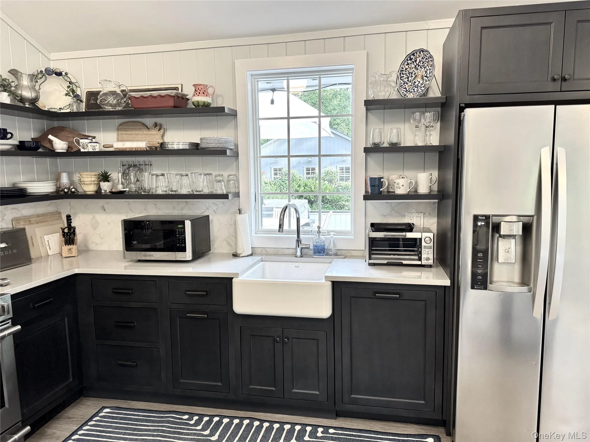 Kitchen with open shelves, dark cabinets, appliances with stainless steel finishes, light stone counters, and backsplash Kitchen with open shelves, dark cabinets, appliances with stainless steel finishes, light stone counters, and backsplash