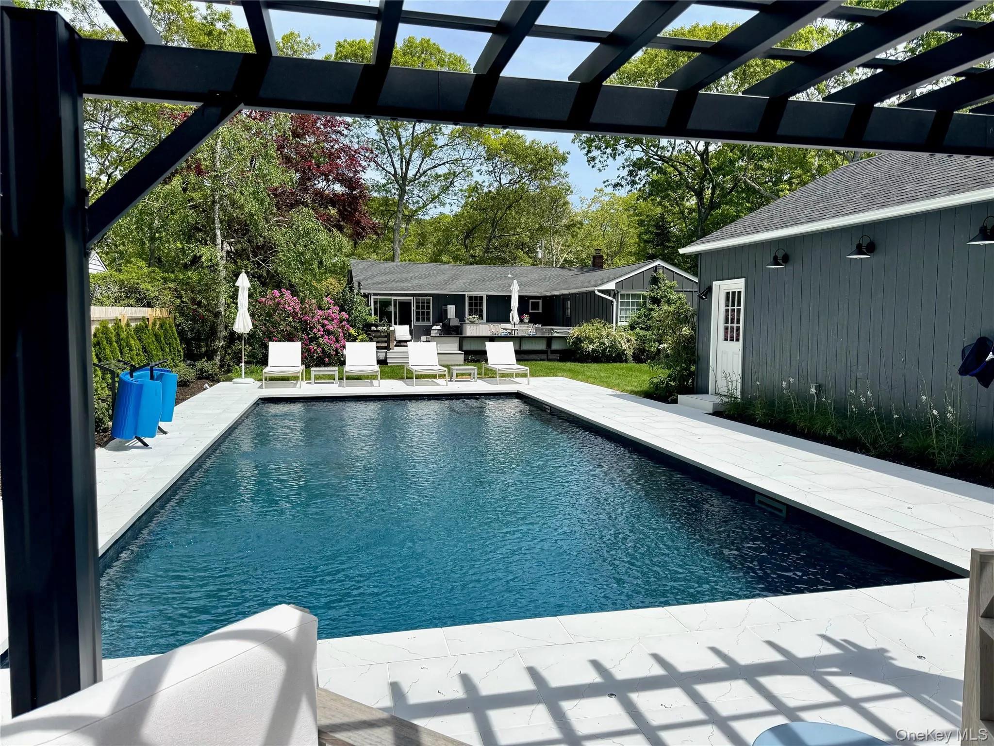 Outdoor pool with a patio area, a pergola, and view of wooded area Outdoor pool with a patio area, a pergola, and view of wooded area