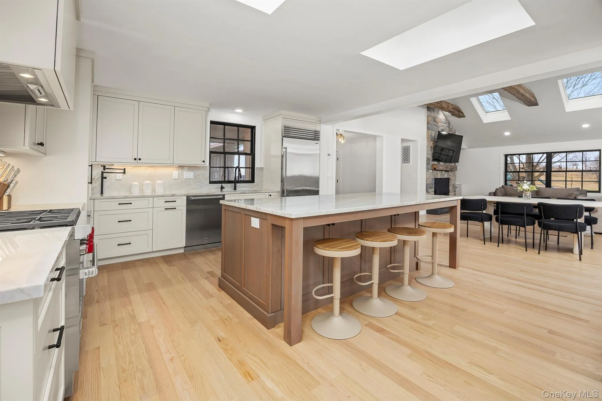 Kitchen featuring a skylight, open floor plan, and light stone counters and counter splash. Kitchen featuring a skylight, open floor plan, and light stone counters and counter splash.