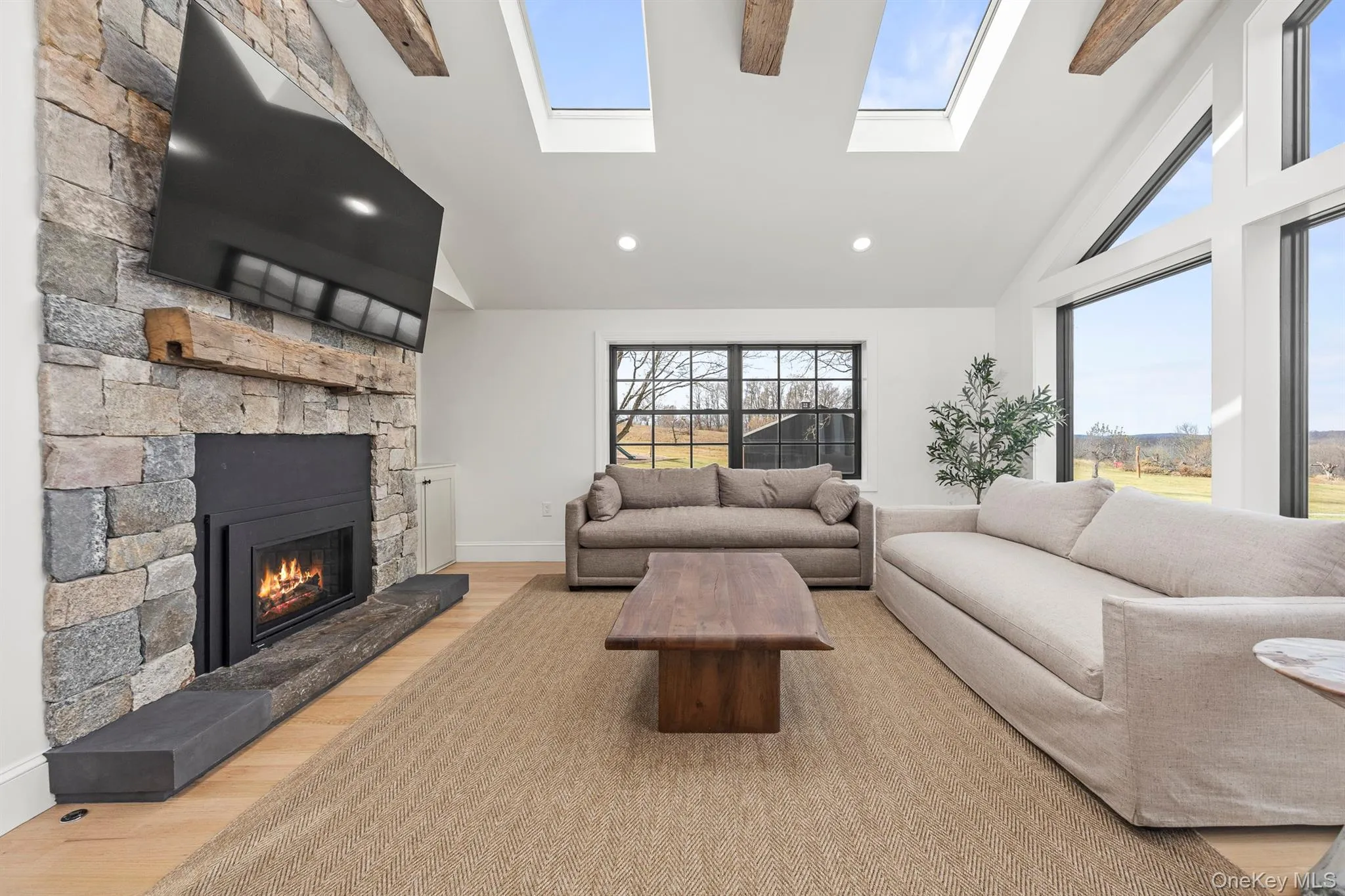 Living room with light wood floors, high vaulted ceiling, a stone fireplace, and a healthy amount of natural light Living room with light wood floors, high vaulted ceiling, a stone fireplace, and a healthy amount of natural light