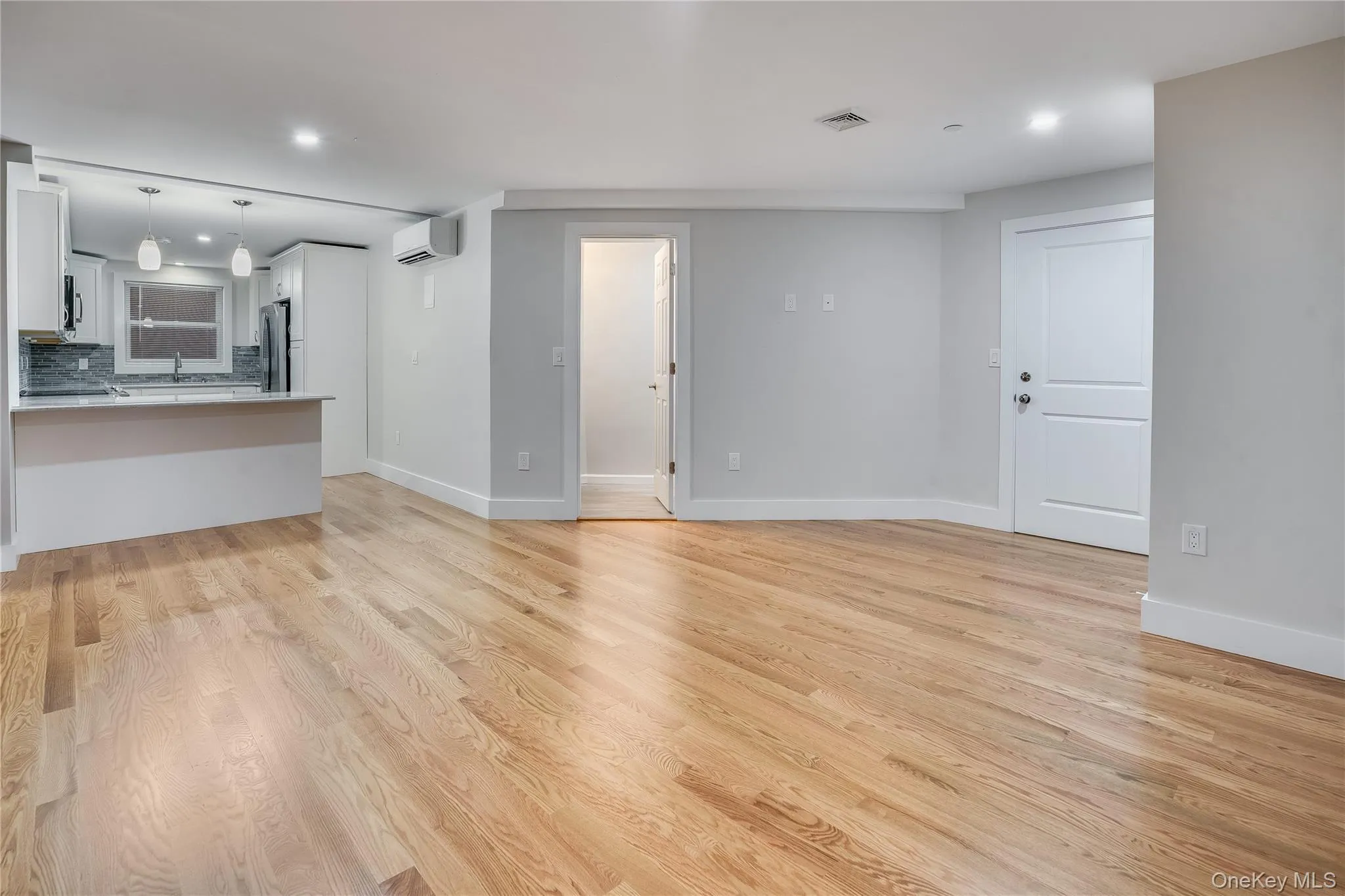 Unfurnished living room featuring recessed lighting, light wood-type flooring, and a wall mounted air conditioner Unfurnished living room featuring recessed lighting, light wood-type flooring, and a wall mounted air conditioner