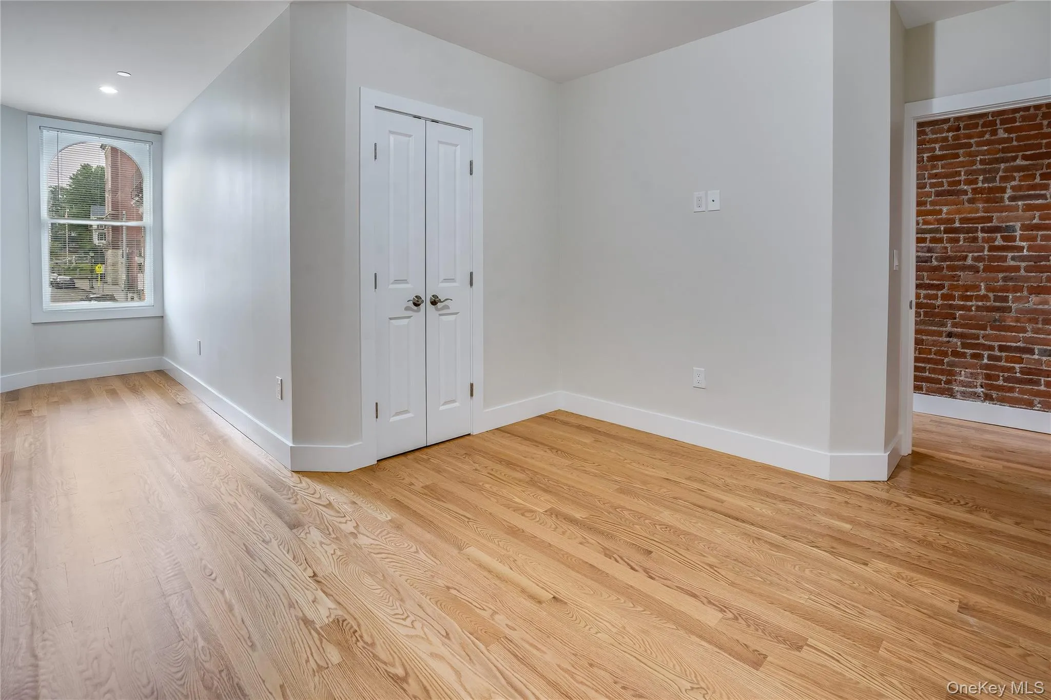 Unfurnished bedroom with light wood-type flooring, a closet, and brick wall Unfurnished bedroom with light wood-type flooring, a closet, and brick wall