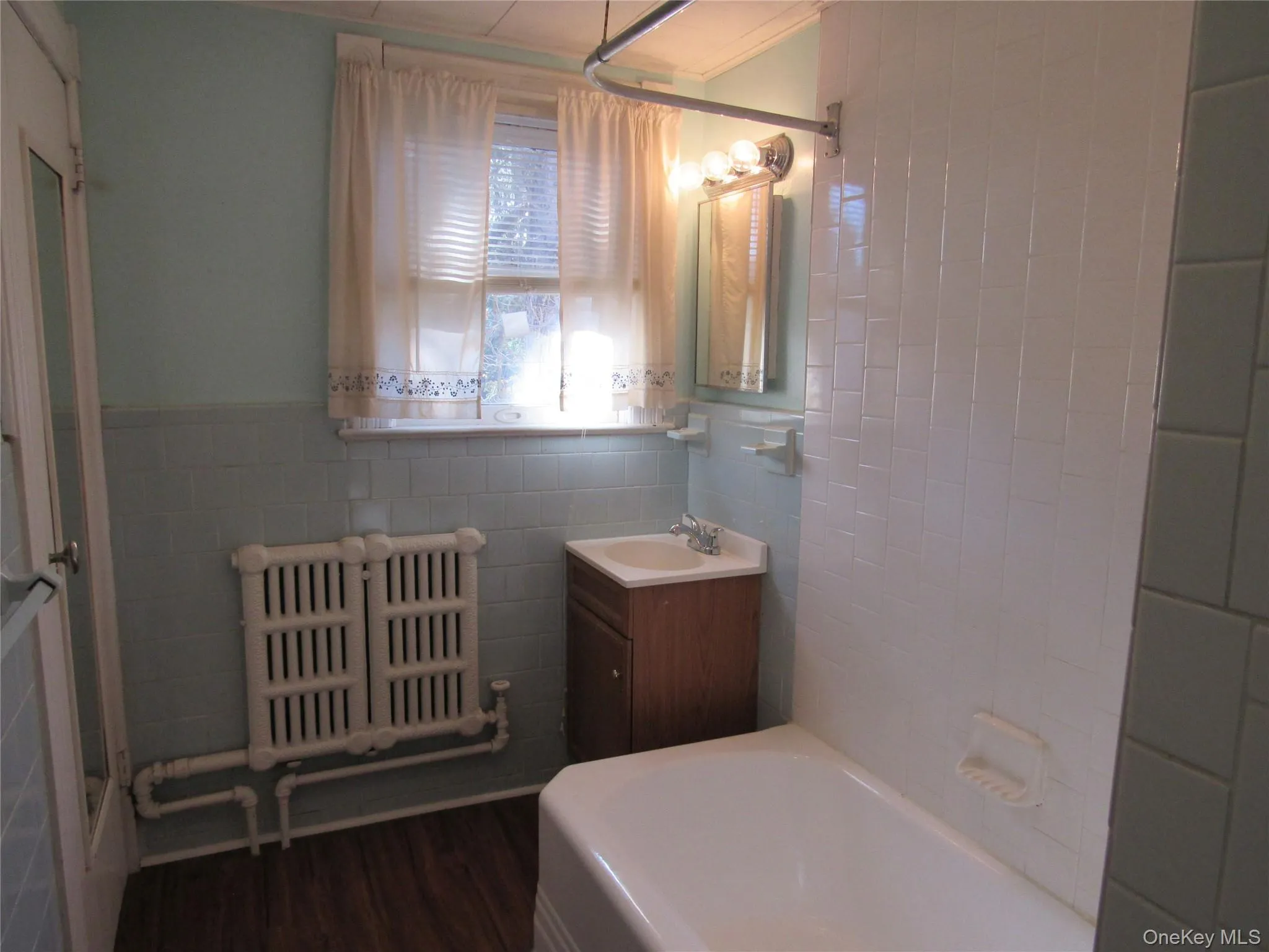 Full bath featuring tile walls, radiator heating unit, vanity, dark wood-style floors, and wainscoting Full bath featuring tile walls, radiator heating unit, vanity, dark wood-style floors, and wainscoting