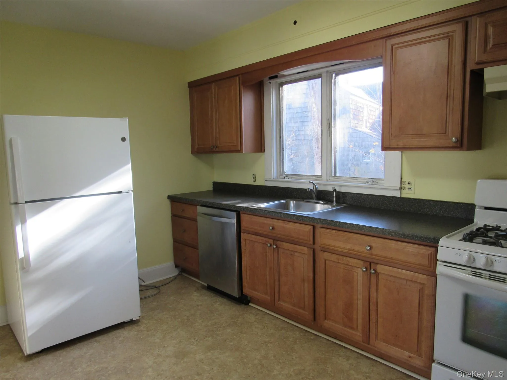 Kitchen featuring brown cabinetry, white appliances, dark countertops, under cabinet range hood, and light floors Kitchen featuring brown cabinetry, white appliances, dark countertops, under cabinet range hood, and light floors