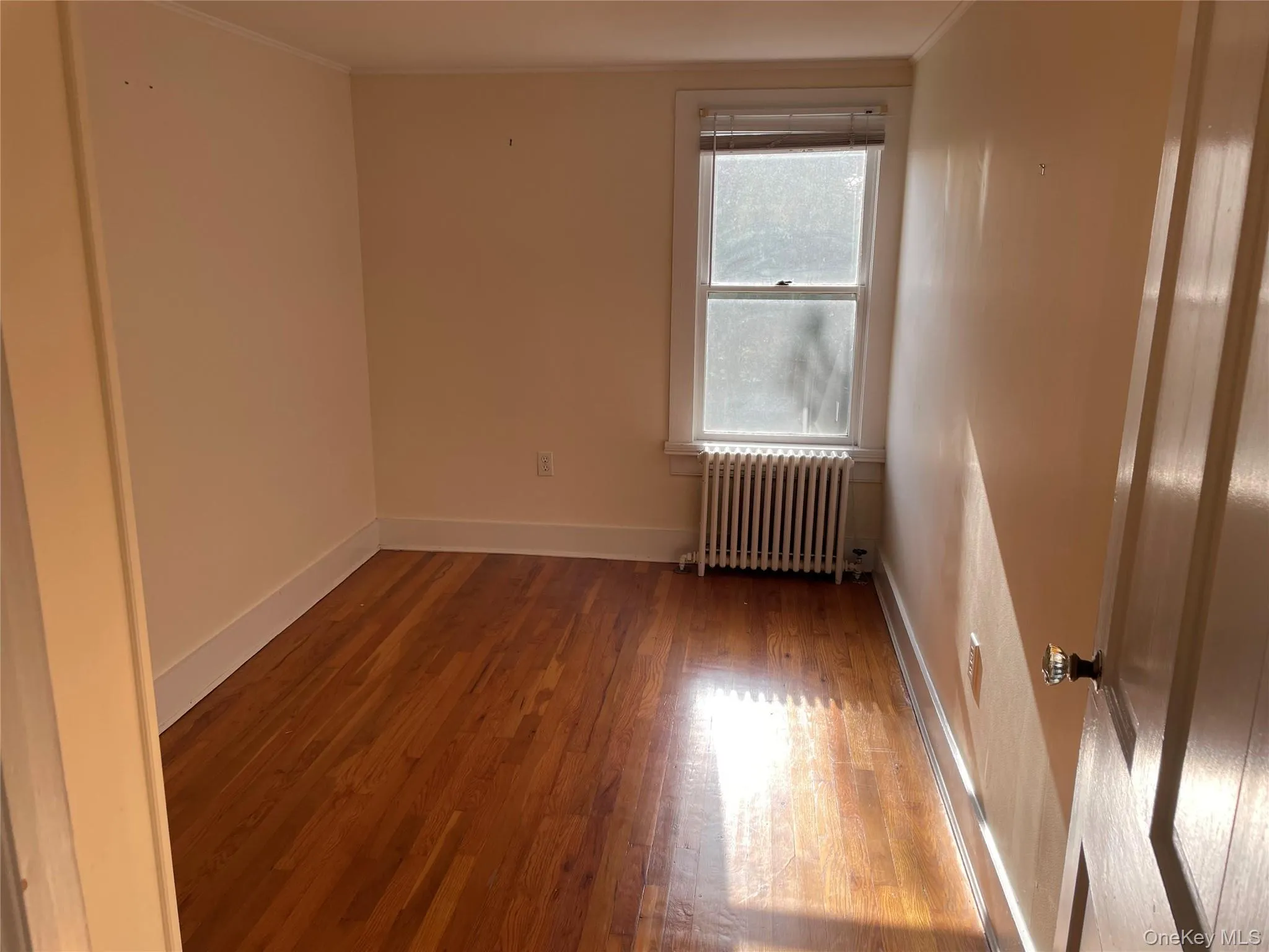 Unfurnished room with radiator, wood finished floors, and ornamental molding Unfurnished room with radiator, wood finished floors, and ornamental molding