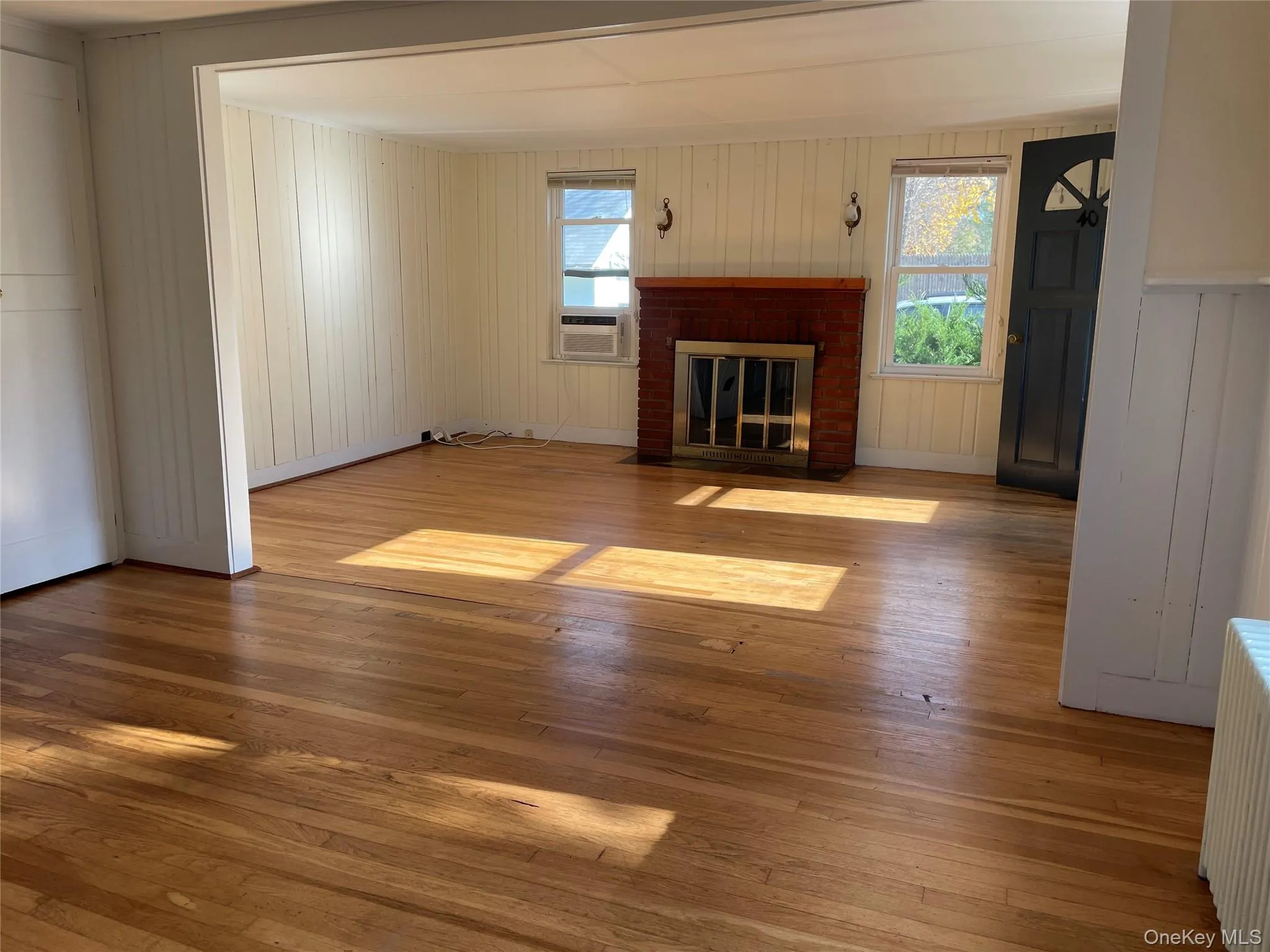 Unfurnished living room featuring hardwood / wood-style floors, radiator heating unit, and a brick fireplace Unfurnished living room featuring hardwood / wood-style floors, radiator heating unit, and a brick fireplace