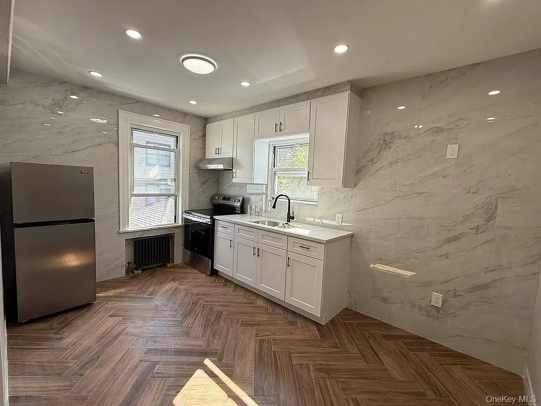 Kitchen with white cabinetry, appliances with stainless steel finishes, radiator, recessed lighting, and under cabinet range hood Kitchen with white cabinetry, appliances with stainless steel finishes, radiator, recessed lighting, and under cabinet range hood