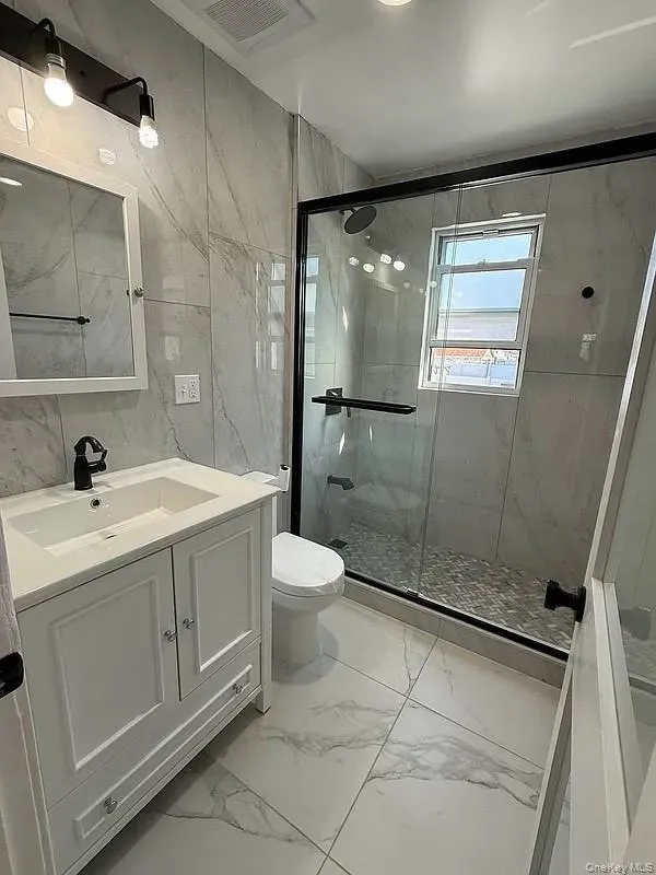 Full bathroom with light marble finish flooring, tile walls, vanity, and a marble finish shower Full bathroom with light marble finish flooring, tile walls, vanity, and a marble finish shower