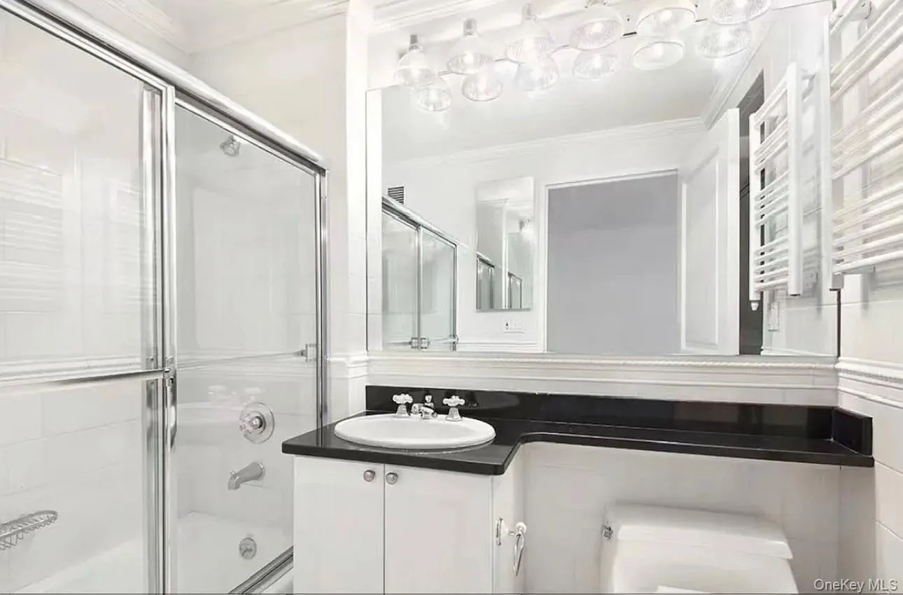 Bathroom featuring bath / shower combo with glass door, radiator heating unit, vanity, crown molding, and a towel warming rack Bathroom featuring bath / shower combo with glass door, radiator heating unit, vanity, crown molding, and a towel warming rack