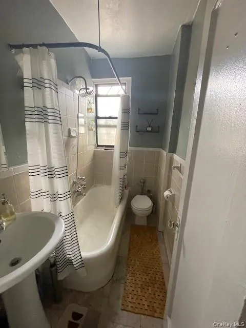 Full bath with tile walls, tile patterned floors, shower / bath combo with shower curtain, and wainscoting Full bath with tile walls, tile patterned floors, shower / bath combo with shower curtain, and wainscoting