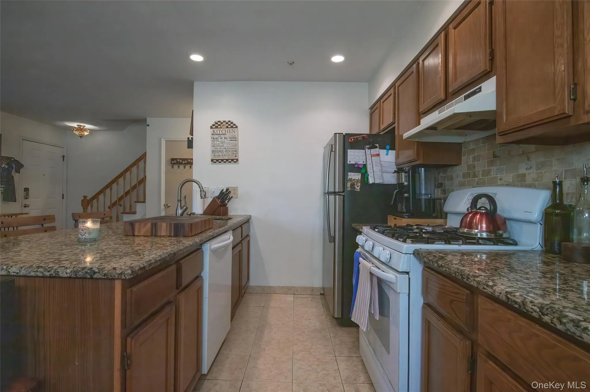 Kitchen featuring white appliances, brown cabinets, under cabinet range hood, dark stone countertops, and a peninsula Kitchen featuring white appliances, brown cabinets, under cabinet range hood, dark stone countertops, and a peninsula