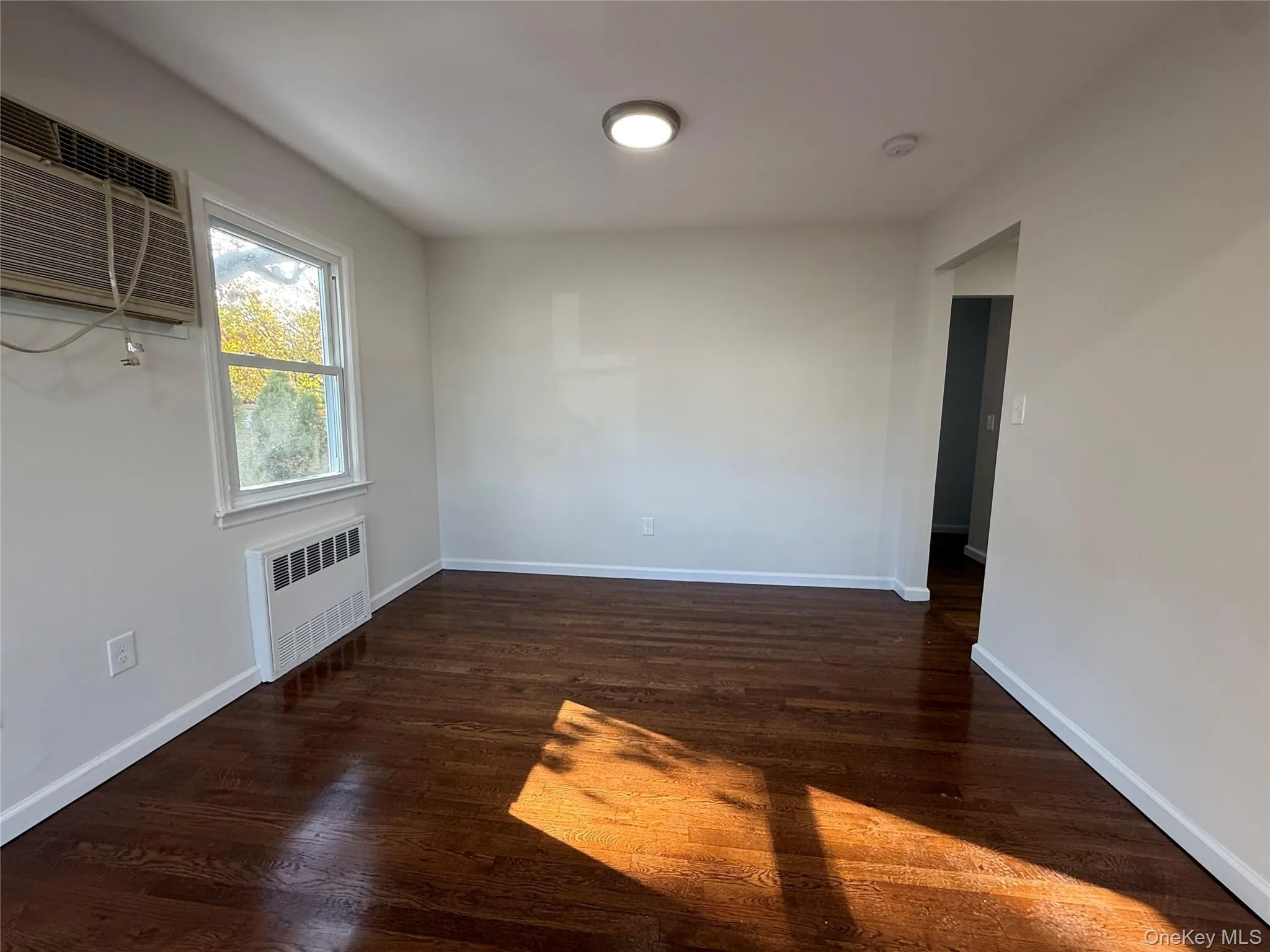Unfurnished room with dark wood-type flooring, radiator, and a wall mounted air conditioner Unfurnished room with dark wood-type flooring, radiator, and a wall mounted air conditioner