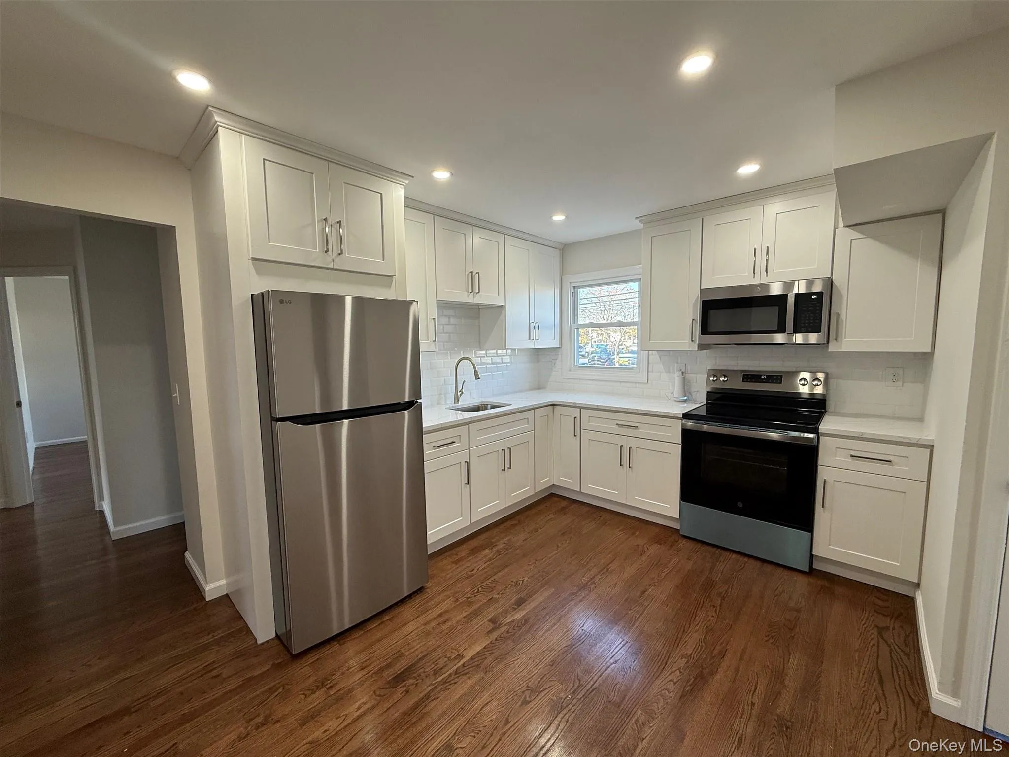 Kitchen with stainless steel appliances, white cabinetry, backsplash, dark wood-type flooring, and recessed lighting Kitchen with stainless steel appliances, white cabinetry, backsplash, dark wood-type flooring, and recessed lighting