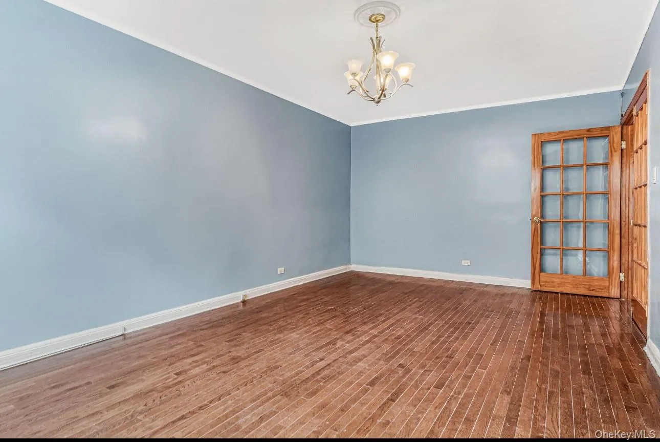 Empty room with a chandelier, dark wood-style floors, and crown molding Empty room with a chandelier, dark wood-style floors, and crown molding