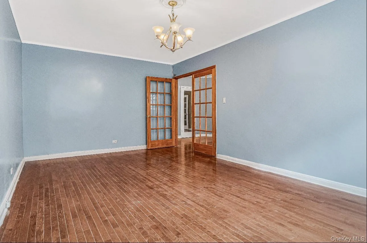 Spare room with crown molding, a chandelier, french doors, and dark wood finished floors Spare room with crown molding, a chandelier, french doors, and dark wood finished floors