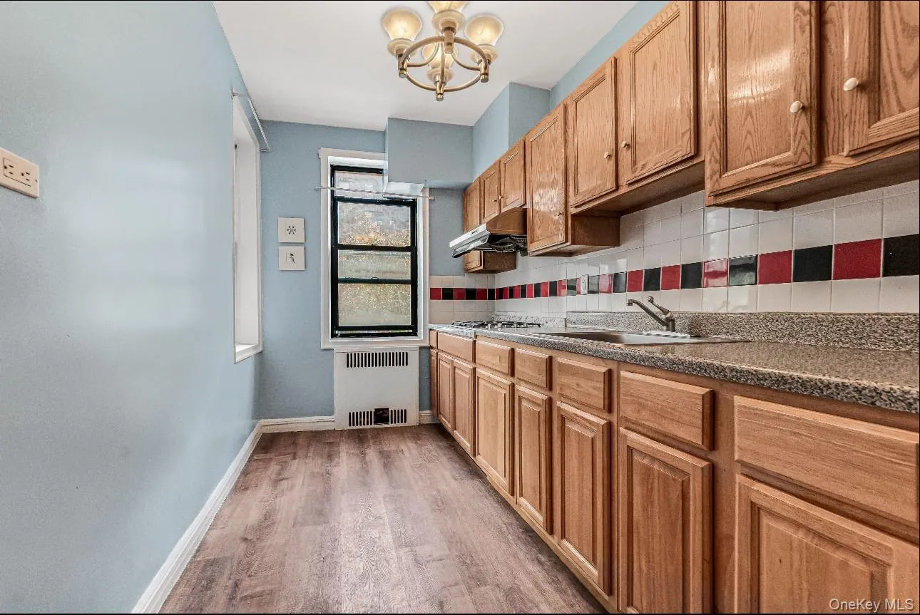 Kitchen featuring tasteful backsplash, a chandelier, light wood-type flooring, radiator, and under cabinet range hood Kitchen featuring tasteful backsplash, a chandelier, light wood-type flooring, radiator, and under cabinet range hood