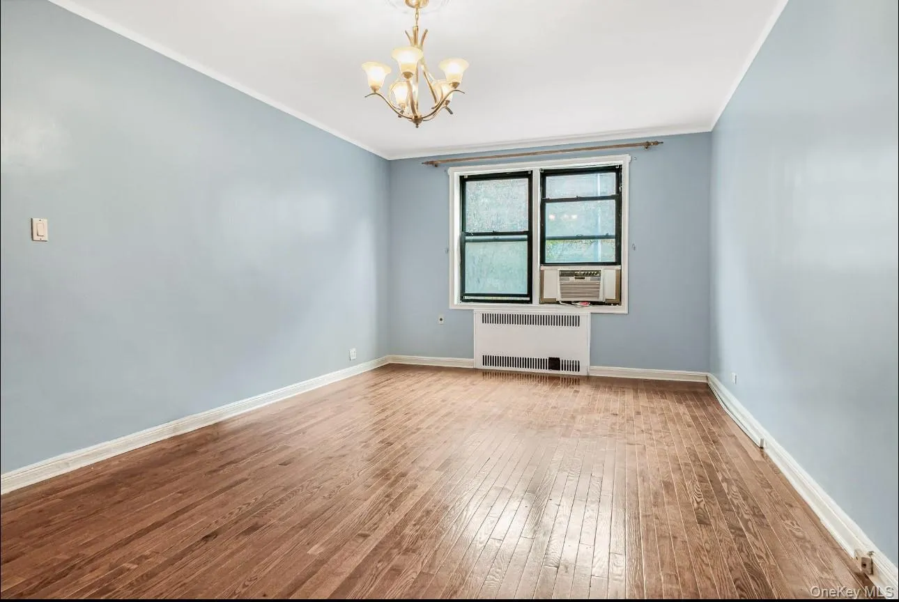 Spare room with radiator, a chandelier, crown molding, and hardwood / wood-style floors Spare room with radiator, a chandelier, crown molding, and hardwood / wood-style floors