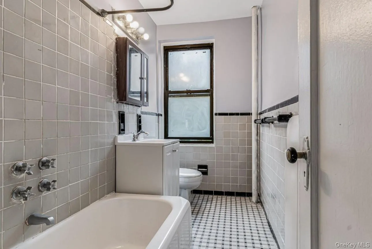 Bathroom featuring vanity, light tile patterned flooring, tile walls, a wainscoted wall, and tub / shower combination Bathroom featuring vanity, light tile patterned flooring, tile walls, a wainscoted wall, and tub / shower combination