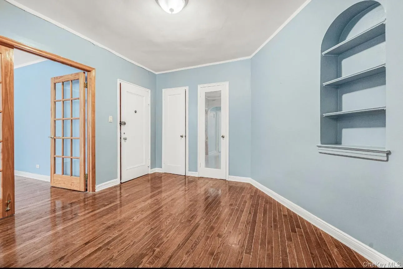 Spare room featuring built in features, dark wood-type flooring, crown molding, and french doors Spare room featuring built in features, dark wood-type flooring, crown molding, and french doors