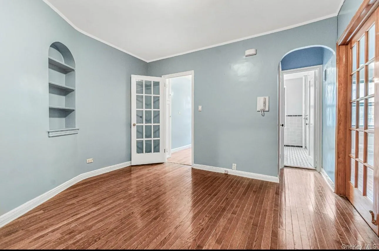 Spare room with arched walkways, ornamental molding, built in shelves, and dark wood finished floors Spare room with arched walkways, ornamental molding, built in shelves, and dark wood finished floors