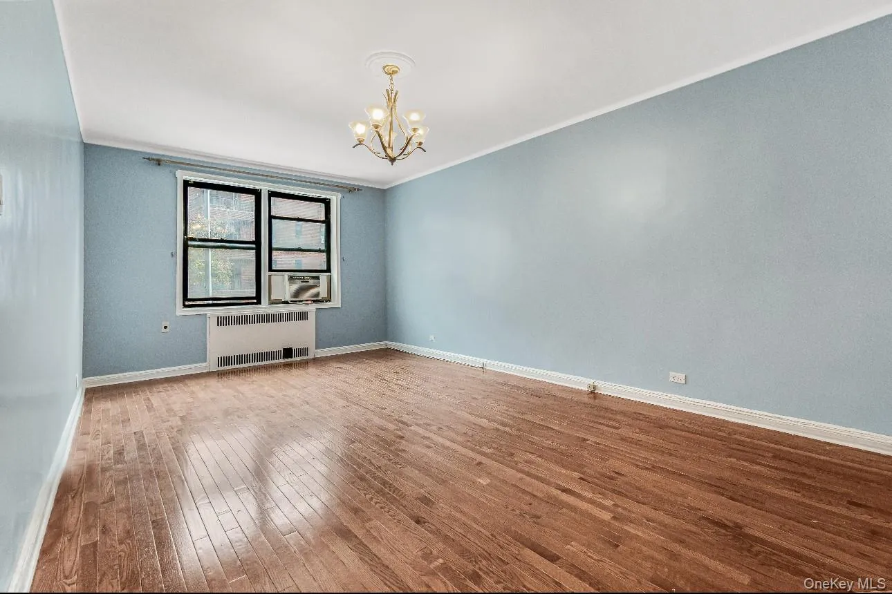 Empty room featuring radiator heating unit, a chandelier, crown molding, and wood-type flooring Empty room featuring radiator heating unit, a chandelier, crown molding, and wood-type flooring