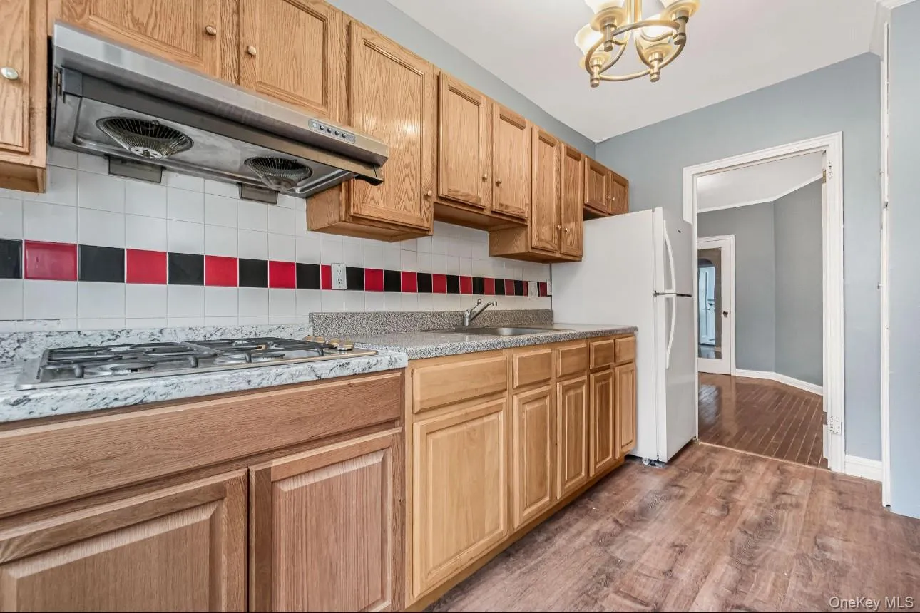 Kitchen with extractor fan, dark wood-type flooring, decorative backsplash, freestanding refrigerator, and a chandelier Kitchen with extractor fan, dark wood-type flooring, decorative backsplash, freestanding refrigerator, and a chandelier