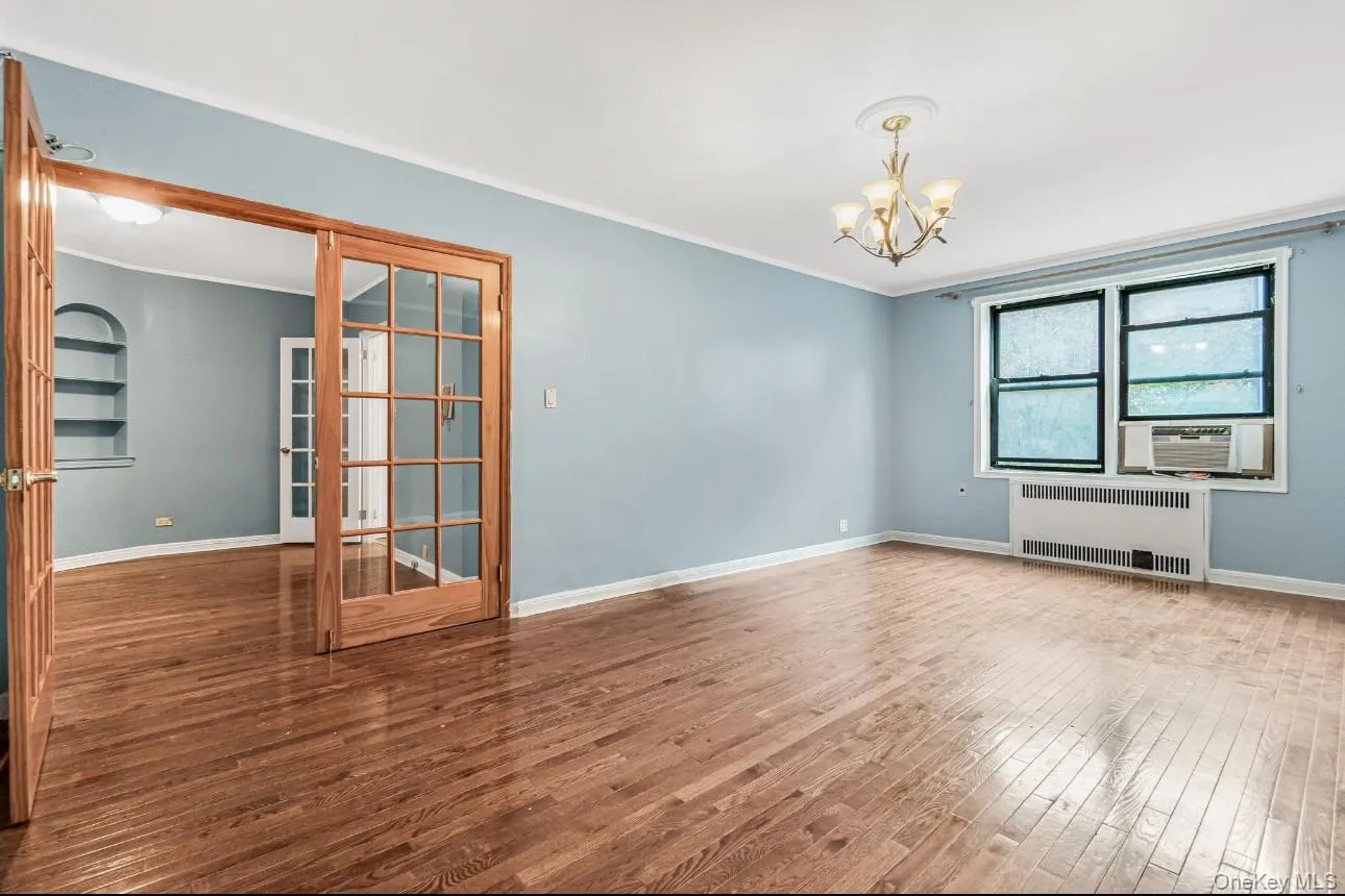 Unfurnished room with radiator heating unit, hardwood / wood-style floors, ornamental molding, and a chandelier Unfurnished room with radiator heating unit, hardwood / wood-style floors, ornamental molding, and a chandelier