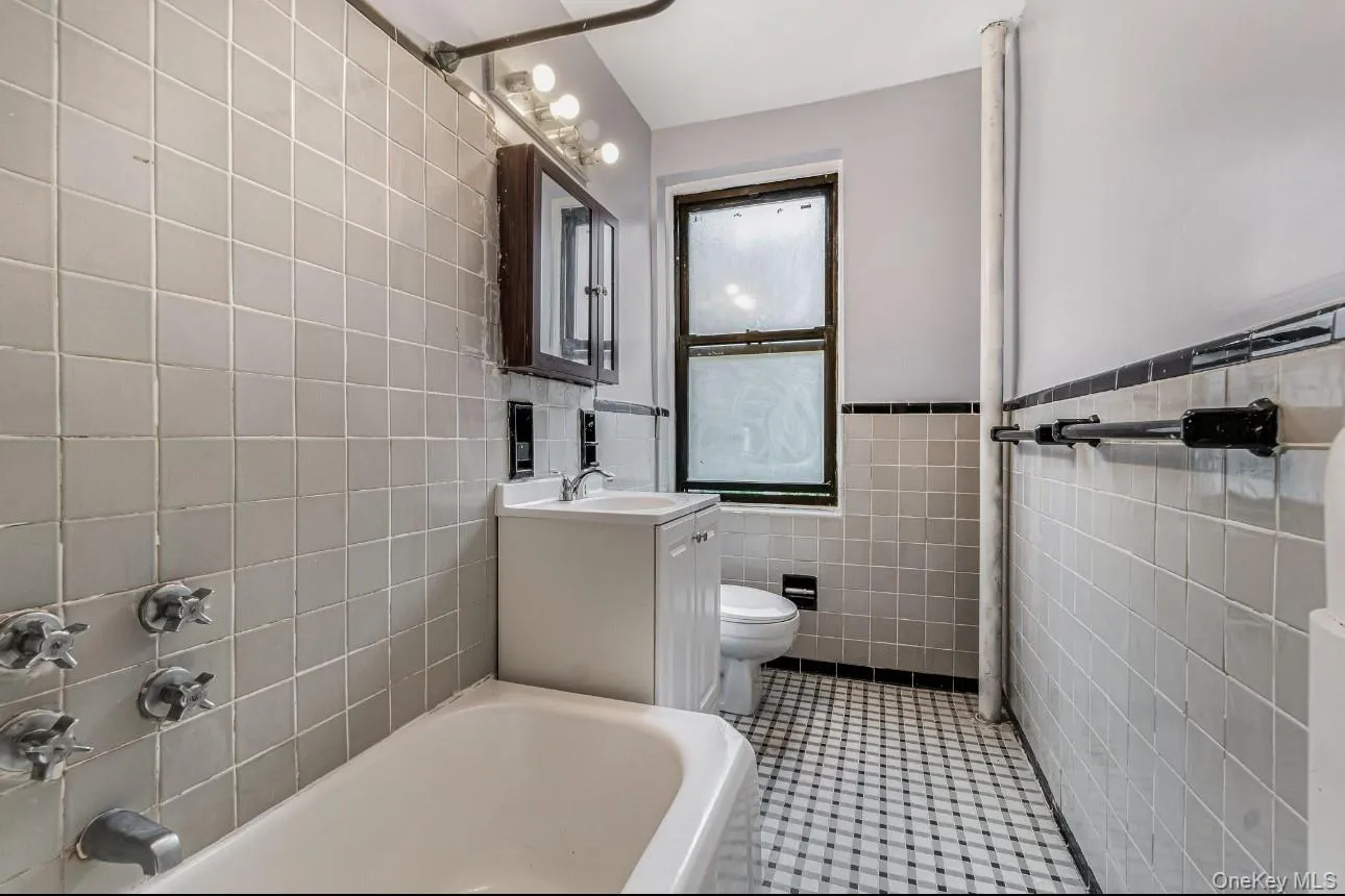 Full bathroom featuring vanity, tile patterned floors, tile walls, and wainscoting Full bathroom featuring vanity, tile patterned floors, tile walls, and wainscoting