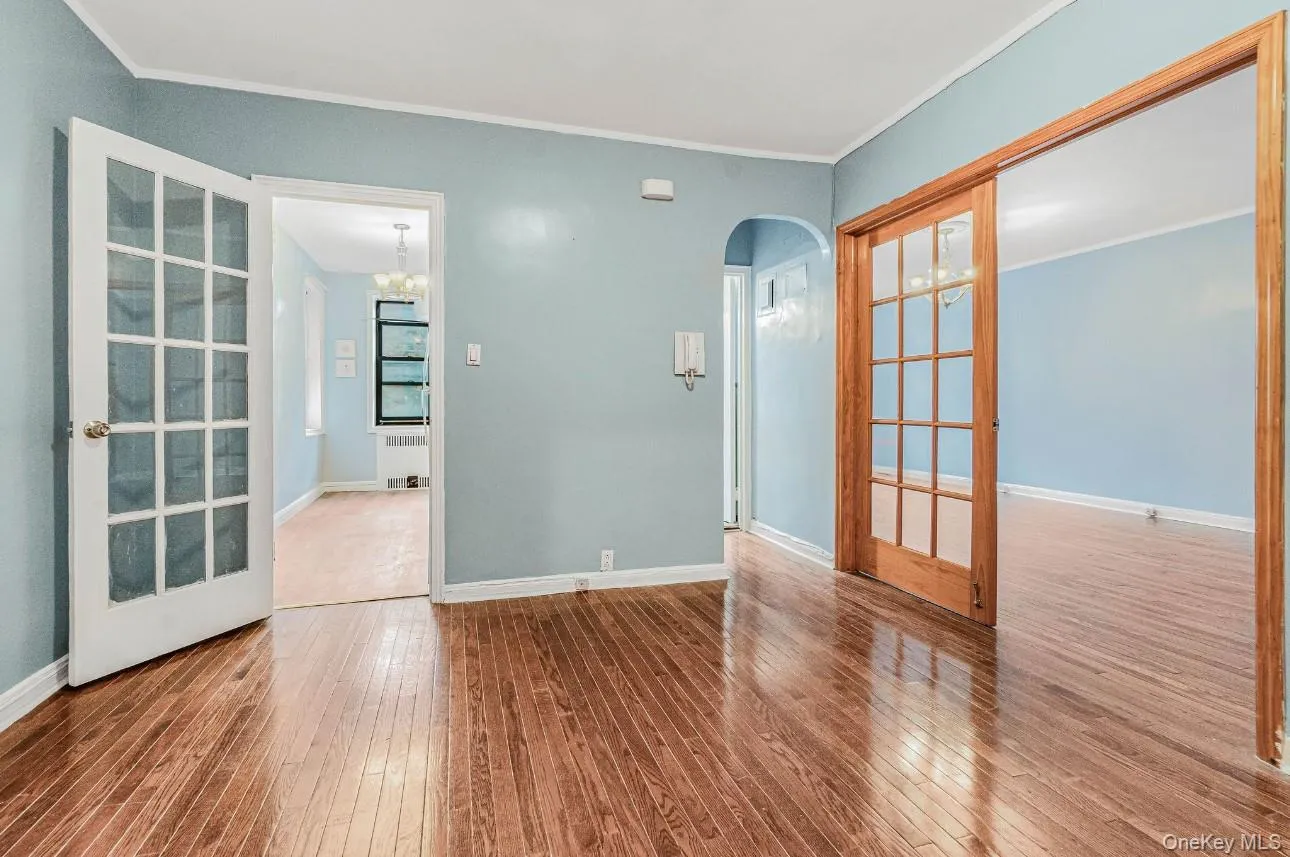Spare room with crown molding, arched walkways, radiator heating unit, hardwood / wood-style flooring, and french doors Spare room with crown molding, arched walkways, radiator heating unit, hardwood / wood-style flooring, and french doors