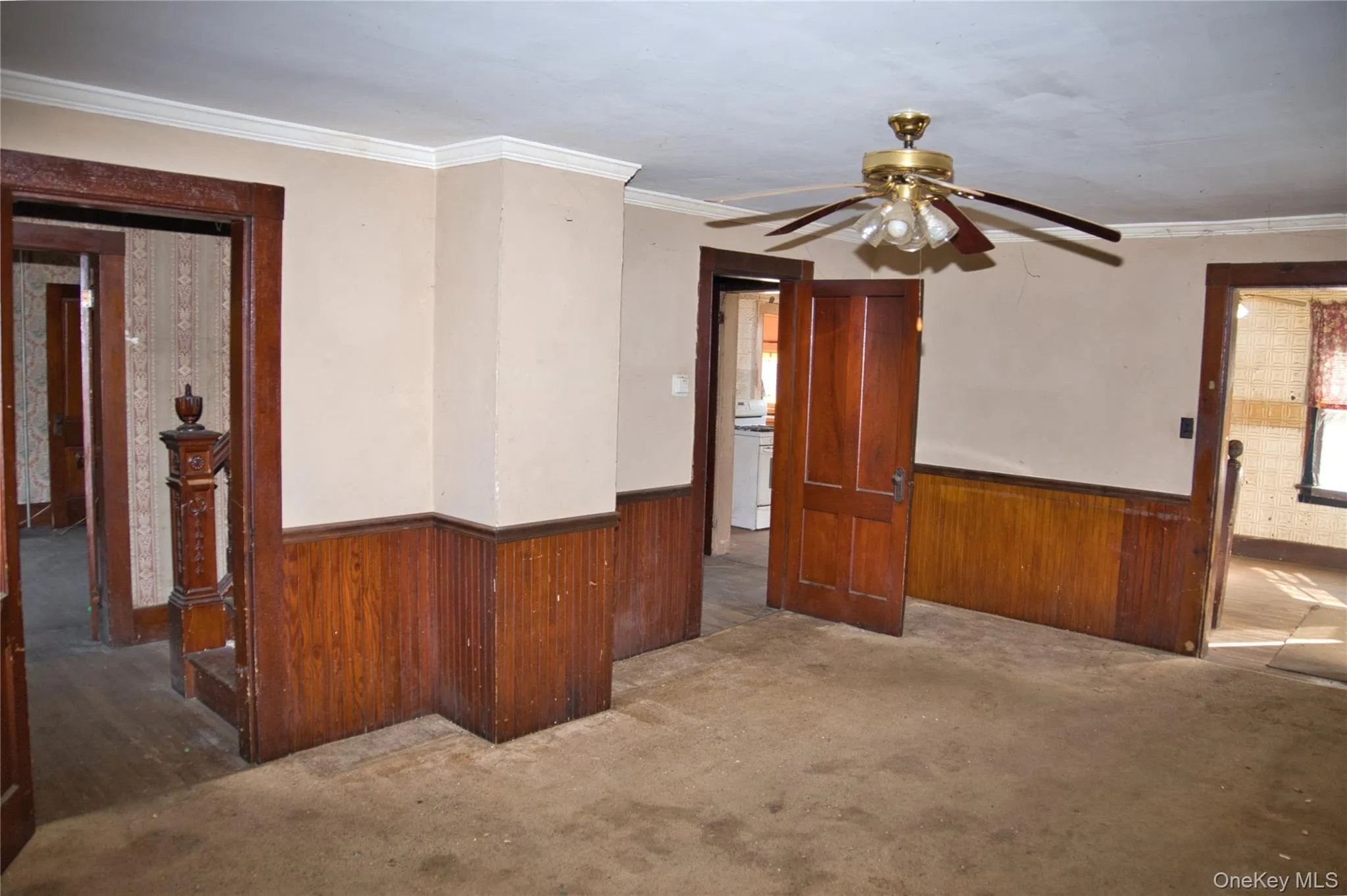 Spare room with a wainscoted wall, wooden walls, ornamental molding, a ceiling fan, and carpet floors Spare room with a wainscoted wall, wooden walls, ornamental molding, a ceiling fan, and carpet floors