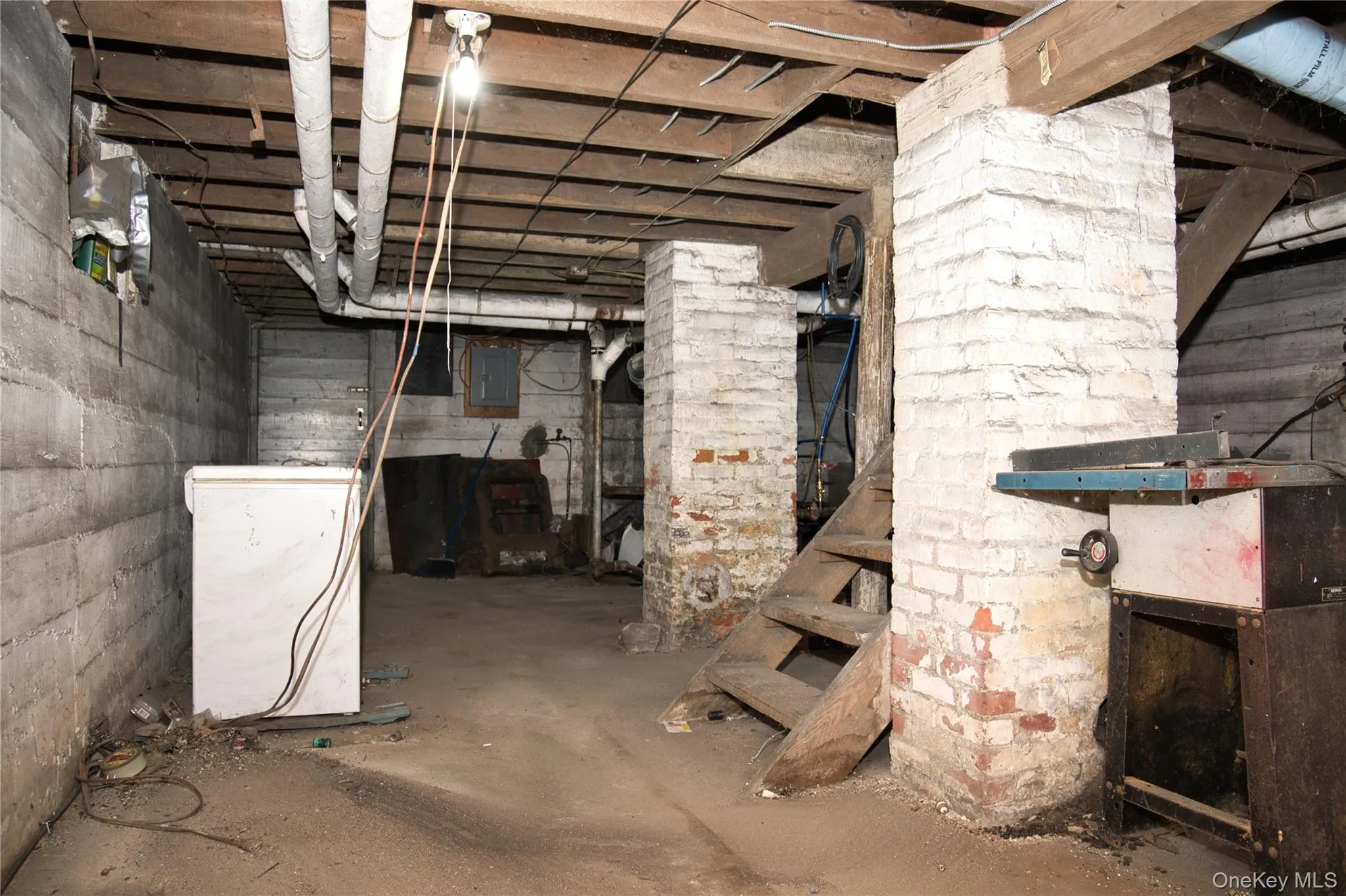 Unfinished below grade area with white refrigerator and electric panel Unfinished below grade area with white refrigerator and electric panel