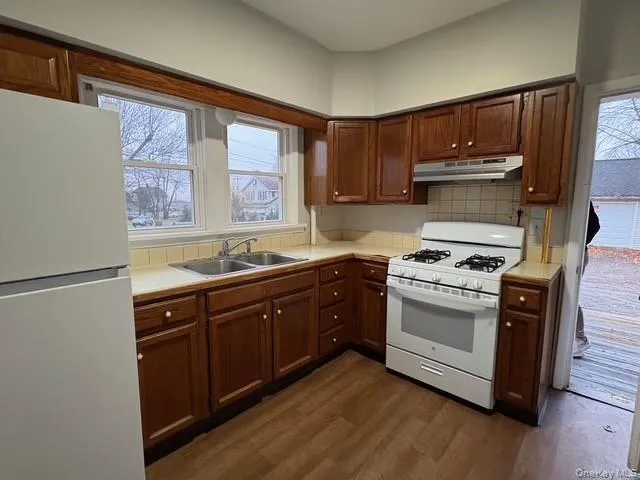Kitchen featuring white appliances, dark wood-type flooring, under cabinet range hood, backsplash, and tile counters Kitchen featuring white appliances, dark wood-type flooring, under cabinet range hood, backsplash, and tile counters