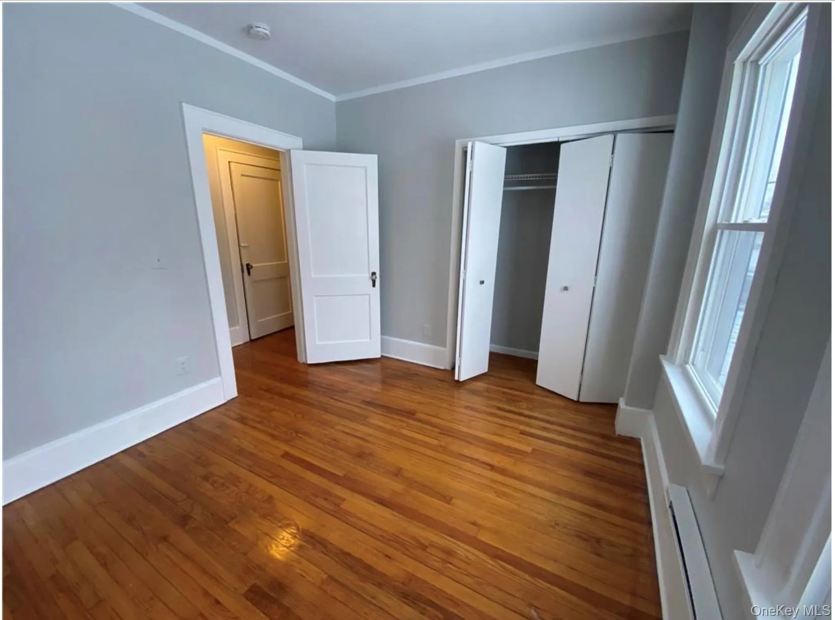 Unfurnished bedroom with hardwood / wood-style flooring, baseboard heating, crown molding, and a closet Unfurnished bedroom with hardwood / wood-style flooring, baseboard heating, crown molding, and a closet