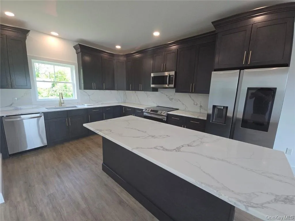 Kitchen featuring light stone countertops, appliances with stainless steel finishes, decorative backsplash, dark wood-type flooring, and recessed lighting Kitchen featuring light stone countertops, appliances with stainless steel finishes, decorative backsplash, dark wood-type flooring, and recessed lighting