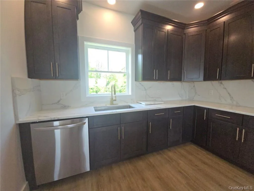 Kitchen with dishwasher, dark wood finished floors, tasteful backsplash, dark brown cabinets, and light stone countertops Kitchen with dishwasher, dark wood finished floors, tasteful backsplash, dark brown cabinets, and light stone countertops