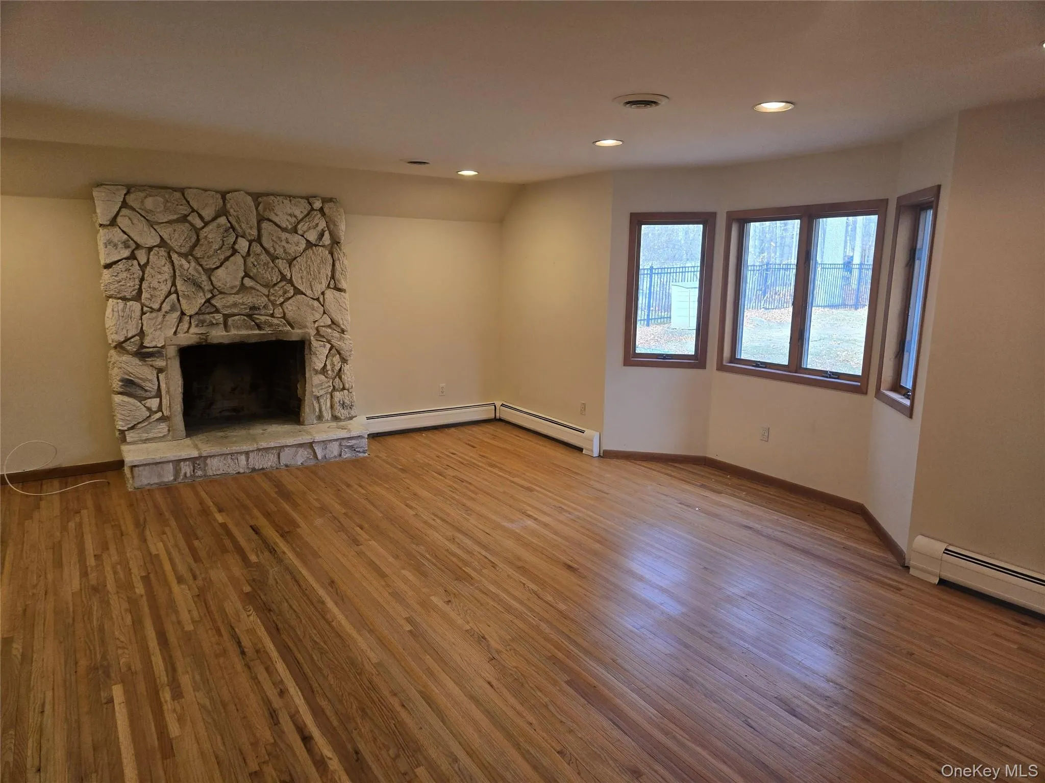 Unfurnished living room with light wood-style flooring, recessed lighting, a stone fireplace, and a baseboard heating unit Unfurnished living room with light wood-style flooring, recessed lighting, a stone fireplace, and a baseboard heating unit