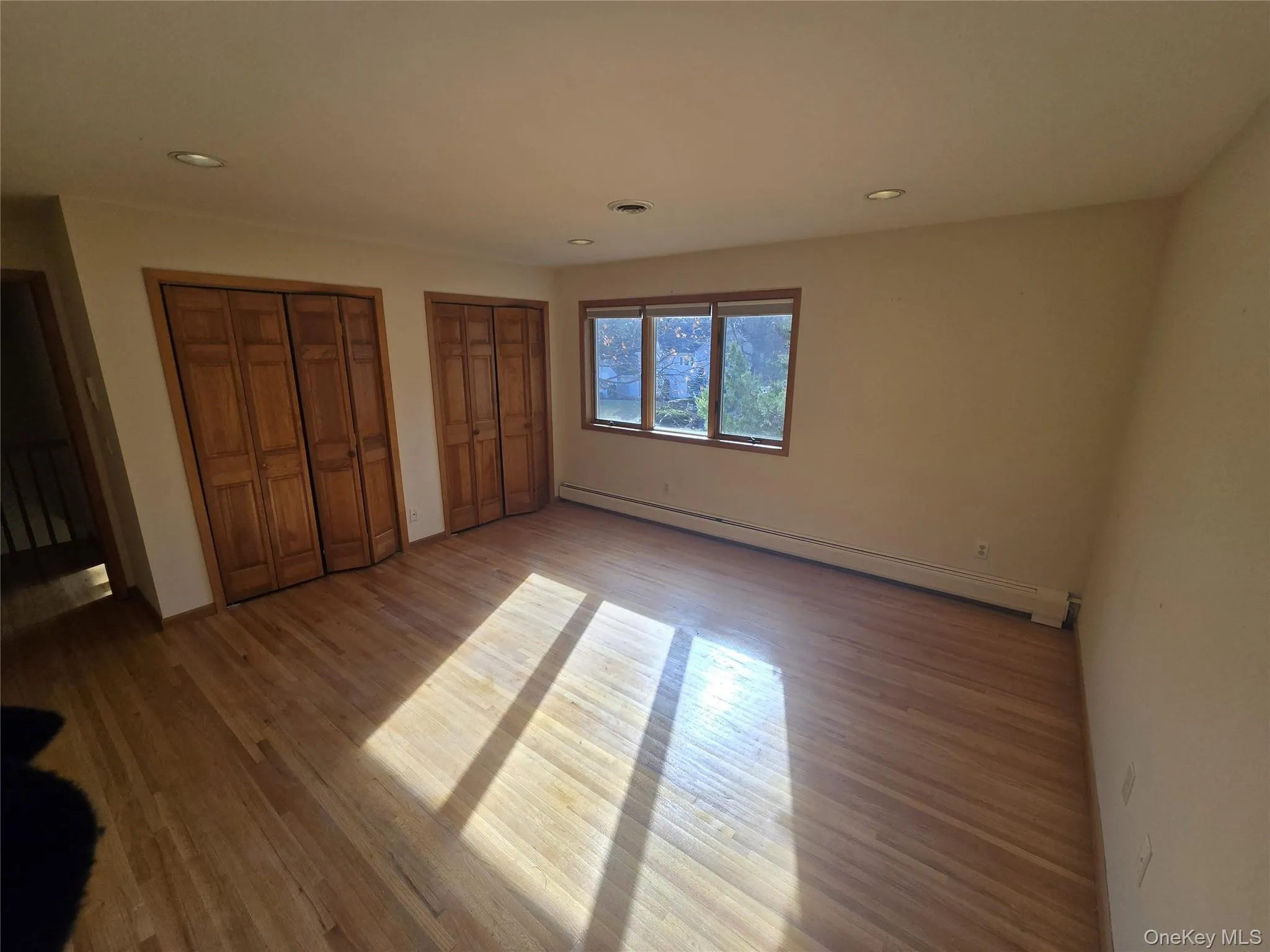 Unfurnished bedroom featuring two closets, a baseboard heating unit, recessed lighting, and wood finished floors Unfurnished bedroom featuring two closets, a baseboard heating unit, recessed lighting, and wood finished floors