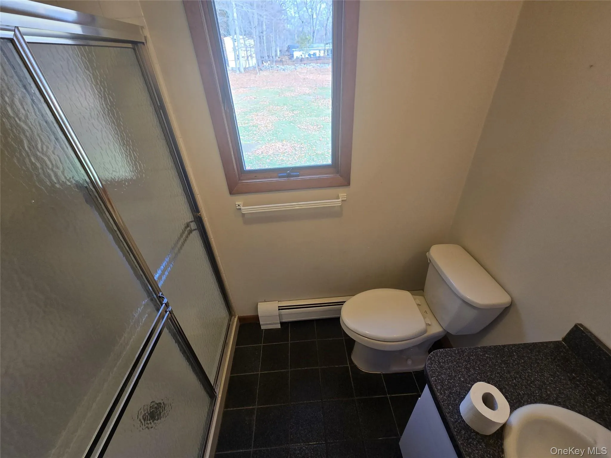 Full bathroom with a stall shower, vanity, baseboard heating, and dark tile patterned flooring Full bathroom with a stall shower, vanity, baseboard heating, and dark tile patterned flooring