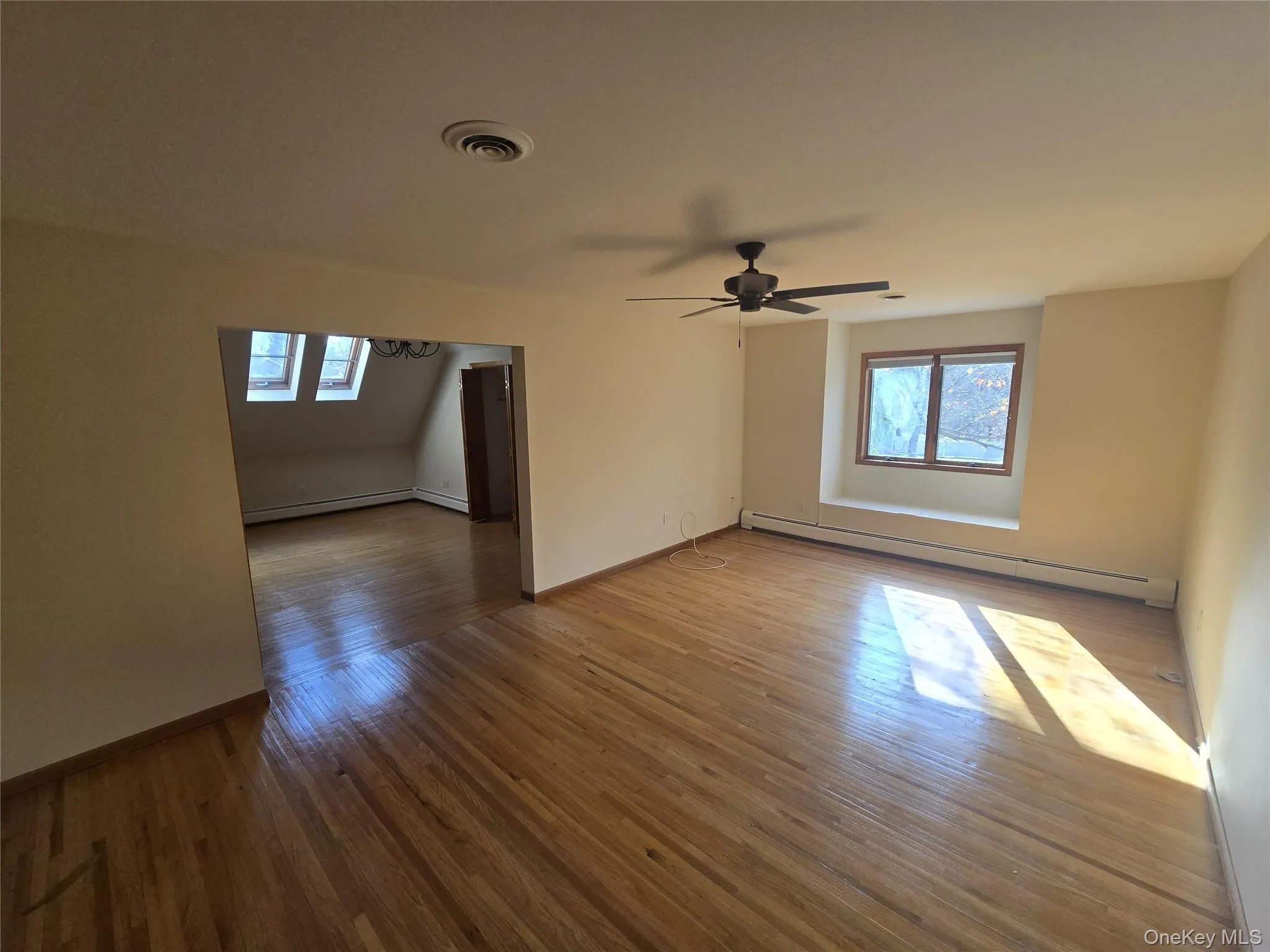 Empty room featuring baseboard heating, dark wood-style floors, and a skylight Empty room featuring baseboard heating, dark wood-style floors, and a skylight