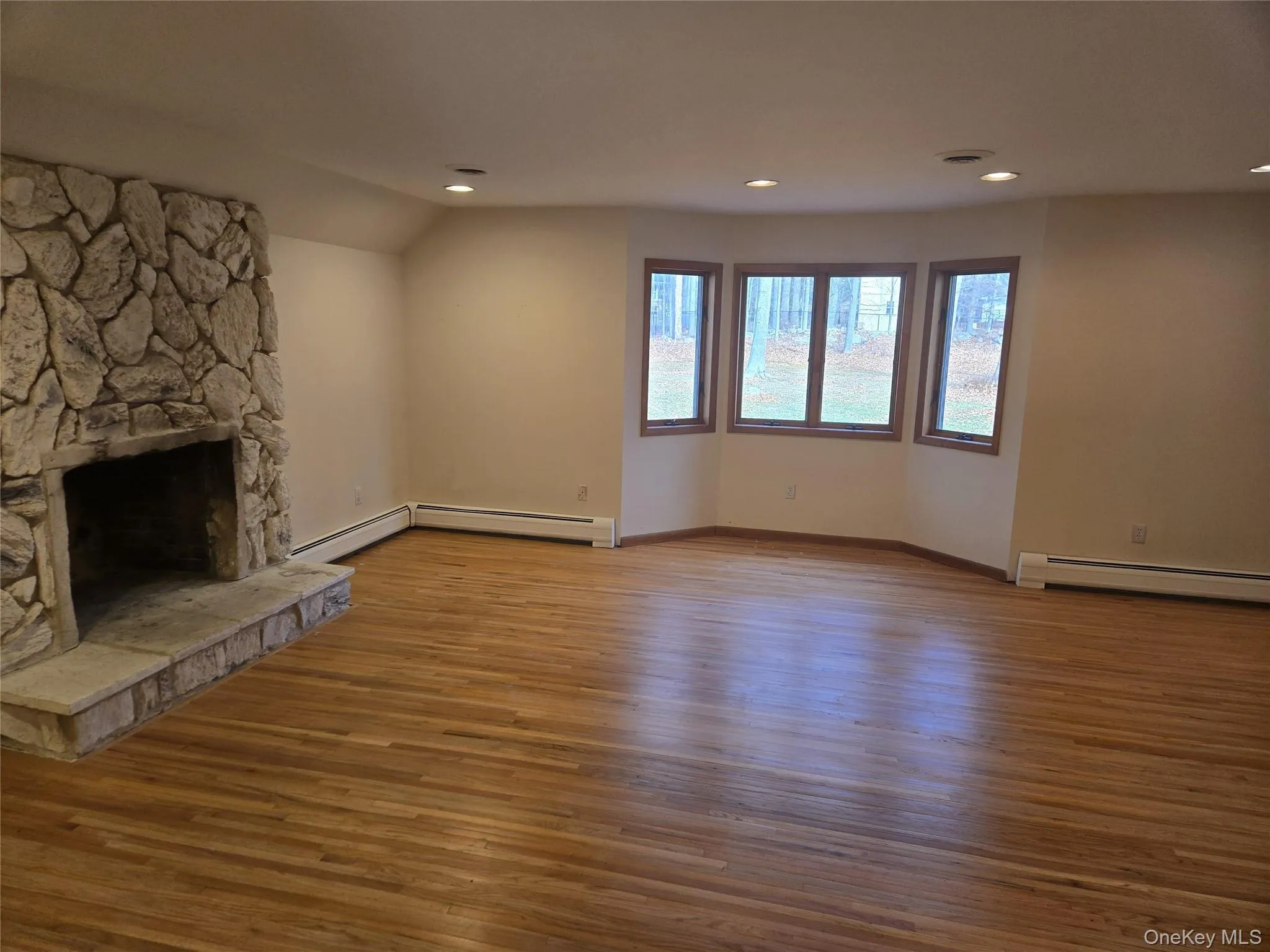 Unfurnished living room featuring a fireplace, light wood-type flooring, recessed lighting, lofted ceiling, and a baseboard heating unit Unfurnished living room featuring a fireplace, light wood-type flooring, recessed lighting, lofted ceiling, and a baseboard heating unit