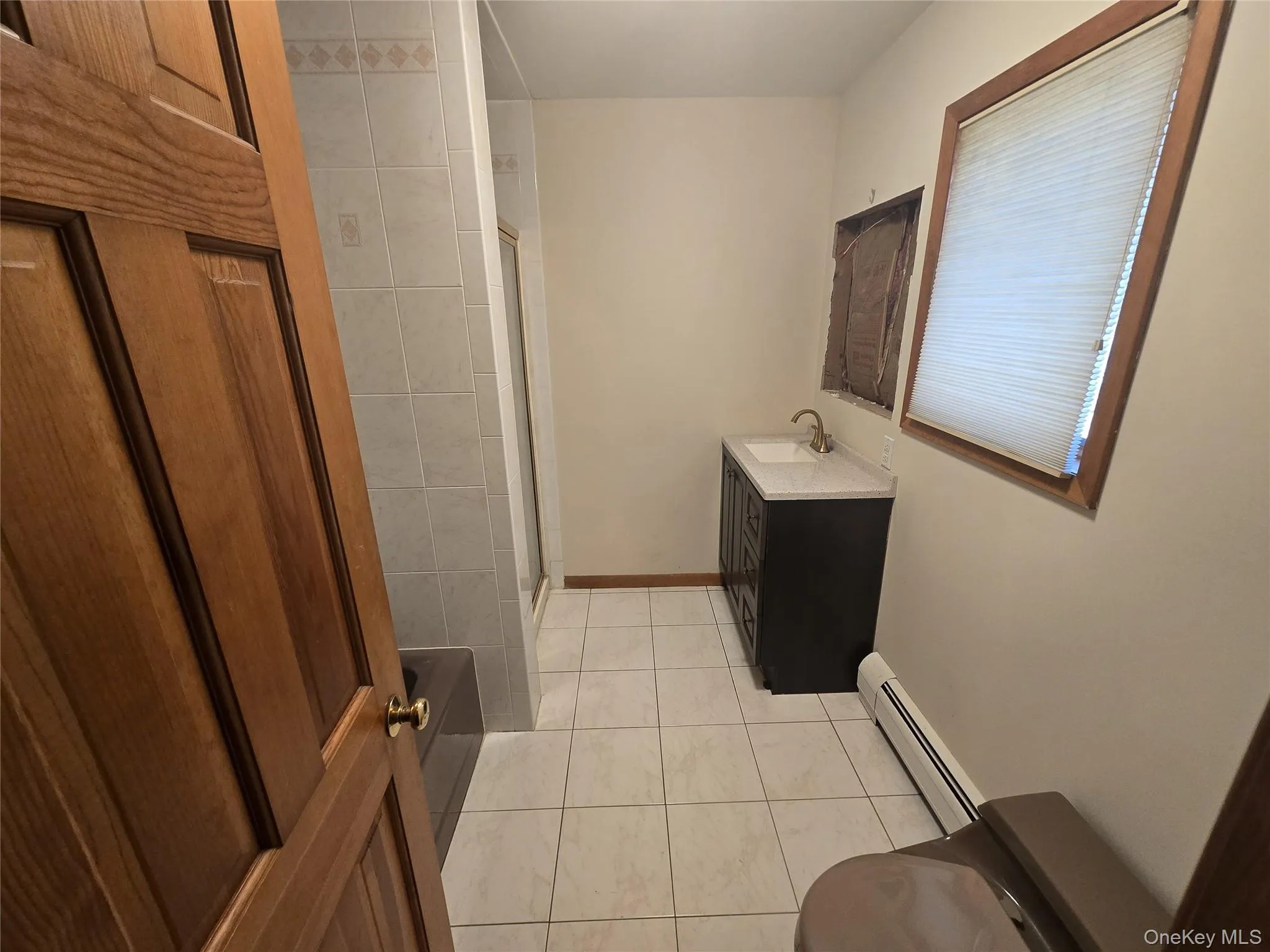Bathroom with light tile patterned floors, a baseboard radiator, vanity, and a shower stall Bathroom with light tile patterned floors, a baseboard radiator, vanity, and a shower stall
