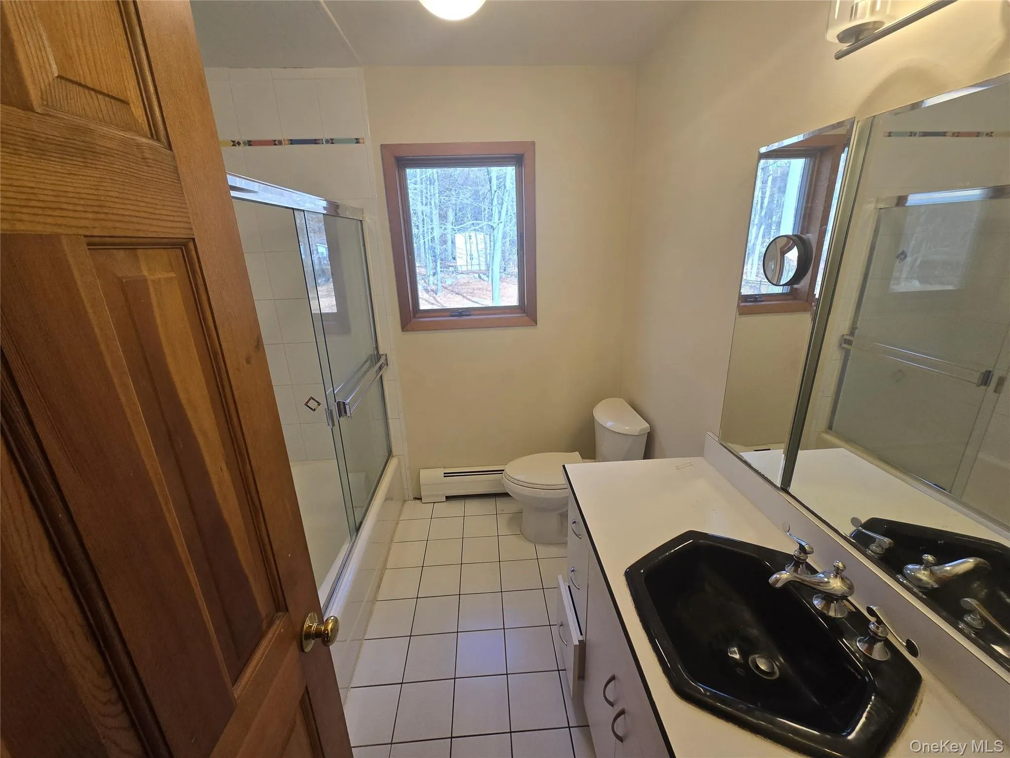 Full bath featuring light tile patterned floors, vanity, a baseboard heating unit, and combined bath / shower with glass door Full bath featuring light tile patterned floors, vanity, a baseboard heating unit, and combined bath / shower with glass door