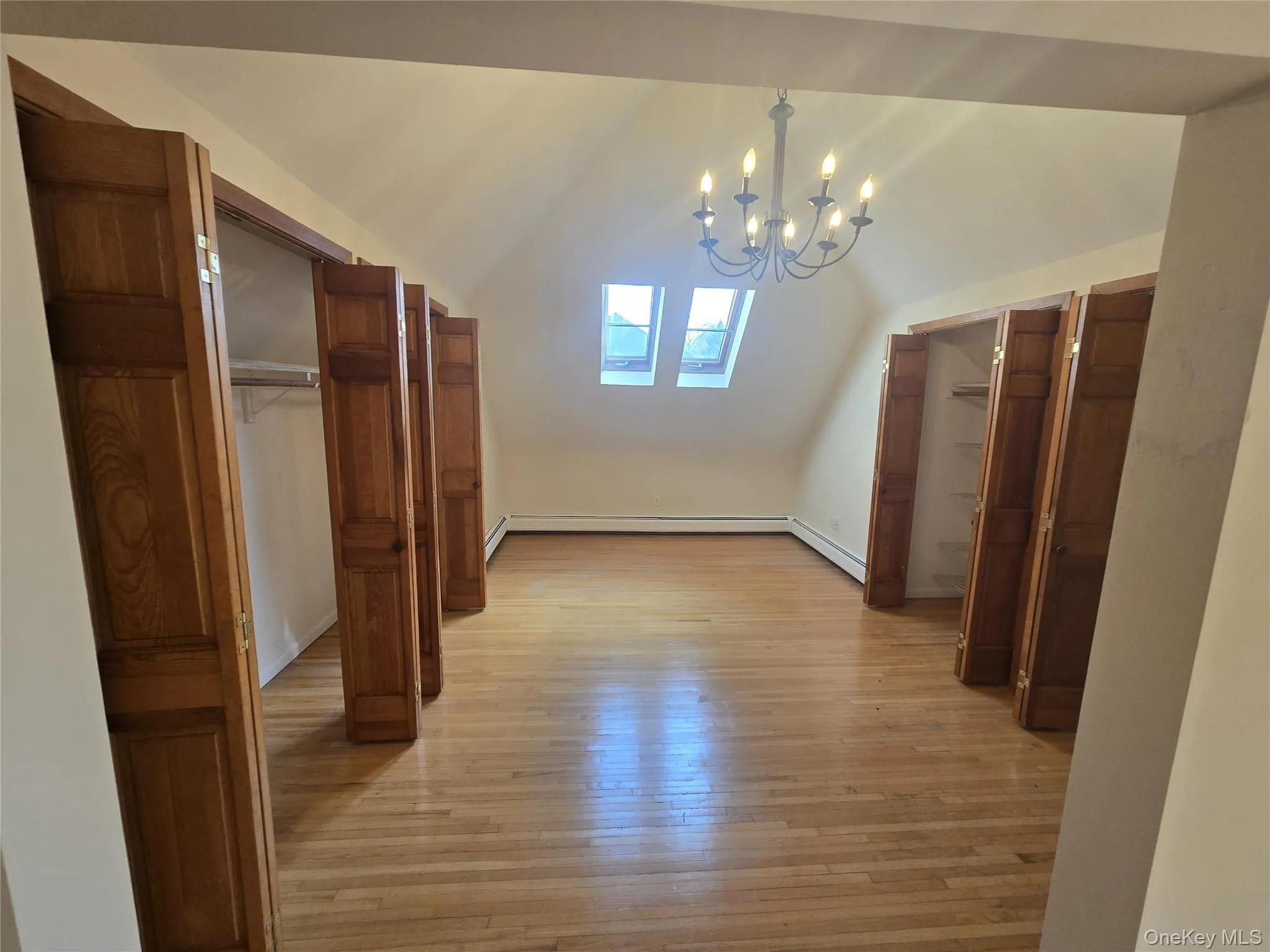 Additional living space in the primary bedroom featuring lofted ceiling, a chandelier, light wood finished floors, a skylight, and baseboard heating Additional living space in the primary bedroom featuring lofted ceiling, a chandelier, light wood finished floors, a skylight, and baseboard heating