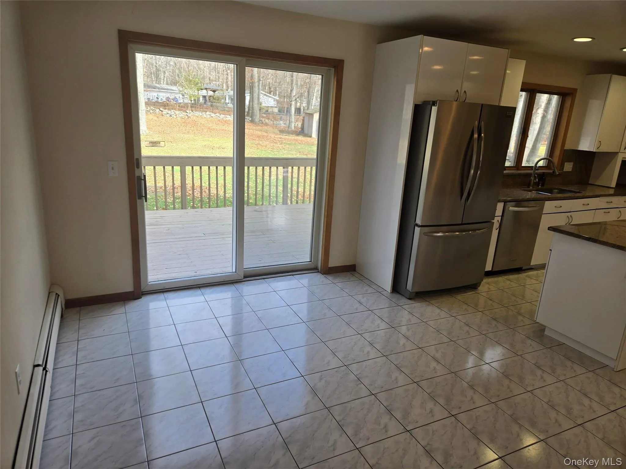 Kitchen with white cabinets, stainless steel appliances, baseboard heating, light tile patterned flooring, and dark stone counters Kitchen with white cabinets, stainless steel appliances, baseboard heating, light tile patterned flooring, and dark stone counters